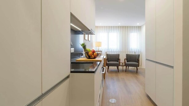 A modern kitchen with a central island, a dining area with two chairs, and a window with curtains.