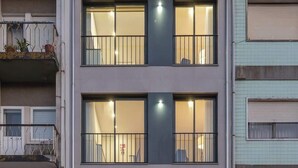 A multi-story residential building with balconies, large windows, and a car parked in front.