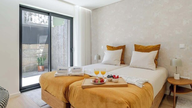 A modern hotel room with a large bed, two pillows, a bedside table with a lamp, and a tray with breakfast. - Stylish Studio w/ Terrace by HostWise (Porto)