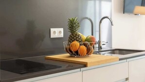 A modern kitchen with a stainless steel sink, a fruit bowl on the countertop, and a wooden cutting board. - Stylish Studio w/ Terrace by HostWise (Porto)
