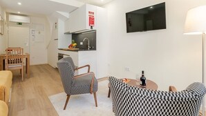 A modern hotel room with a kitchenette, a dining area, a TV mounted on the wall, and a sofa. - Stylish Studio w/ Terrace by HostWise (Porto)