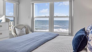 Une chambre à coucher comprenant un lit, une chaise, une commode et une grande fenêtre donnant sur la mer.