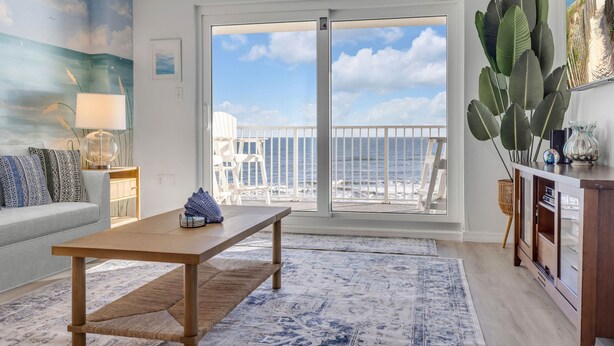 Un salon avec une grande fenêtre, un canapé, une table en bois et une vue sur la plage.