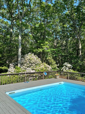 A swimming pool surrounded by a wooden deck and lush greenery.