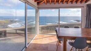 A spacious balcony with a wooden table and chairs, large sliding glass doors, and a view of the ocean.