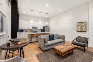 A modern kitchen with white cabinets, a dining area with a round table, and a gray sofa. - The Saddlery-Southern Set-2 Units-Walk to Broadway (Nashville)