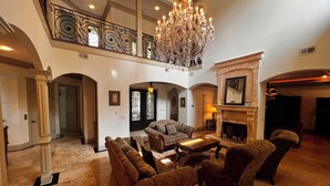 Un salón amplio con techo alto, un candelabro, una chimenea y una escalera que lleva a un nivel superior.