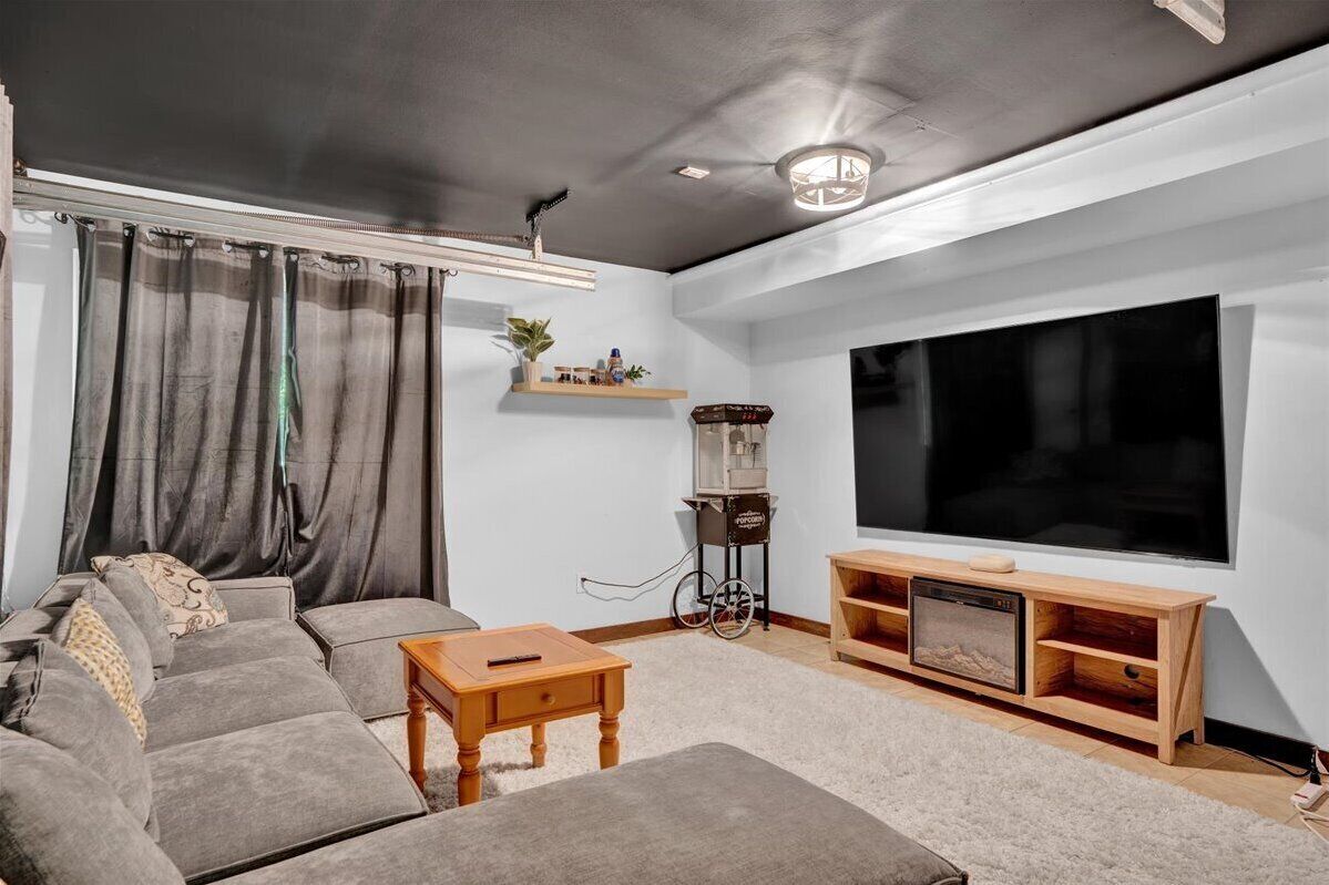 Een moderne woonkamer met een grijze bank, een houten salontafel, een televisie op een houten dressoir, en een popcornmachine.
