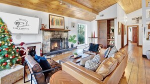 A spacious living room with a fireplace, leather sofas, and a Christmas tree.