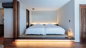 A modern bedroom with a bed centered on a platform, a bedside table, and a wall-mounted light fixture. - Kaigyokutei-Megumi- (Sakaiminato)