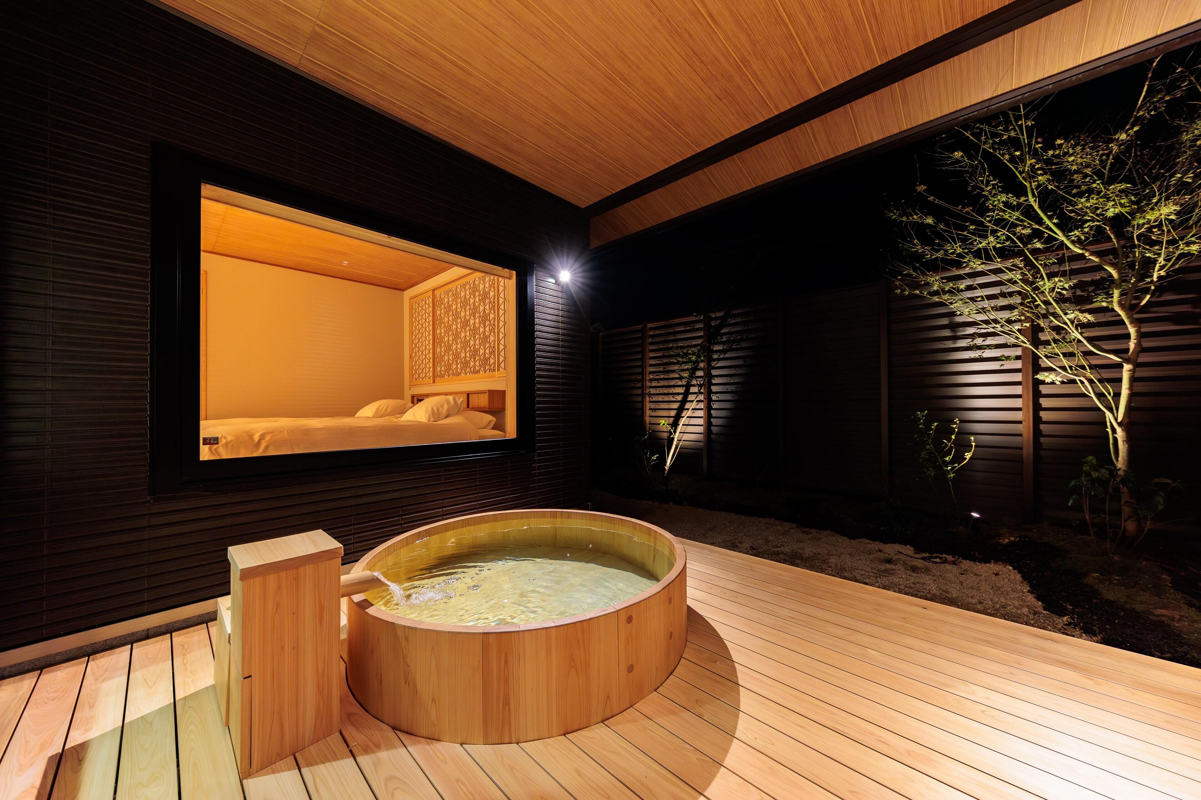 Ein moderner Wellnessbereich mit einem Holz-Hottub, einem Massageroom und Blick auf einen Baum.