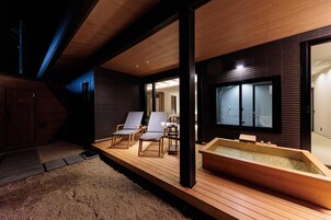 Una terraza de madera con un jacuzzi, dos sillones de descanso y vista a una habitación tradicional japonesa.