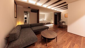 A modern living room with a sectional sofa, a round wooden coffee table, and a bed in the background. - Kaigyokutei-Megumi- (Sakaiminato)