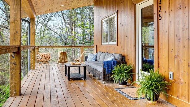 A wooden deck with a sofa and a table, surrounded by potted plants.