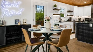 A modern kitchen with white cabinets, a neon sign reading "Starlit Retreat", and a dining area with a round table and brown chairs.