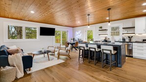 A modern kitchen with a central island, wooden ceiling, and large windows.