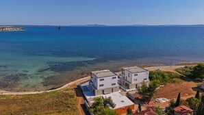 Une propriété située sur la côte, comprenant deux bâtiments modernes, offrant une vue dégagée sur la mer et un chemin de terre menant à la plage.
