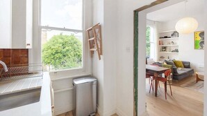 A modern kitchen with a window, a small trash bin, and a dining area with a table and chairs. - GuestReady - Stylish & Spacious 1bed in Islington (London)
