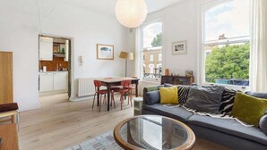 A modern living room with a sofa, a glass coffee table, and a dining area with a table and chairs. - GuestReady - Stylish & Spacious 1bed in Islington (London)