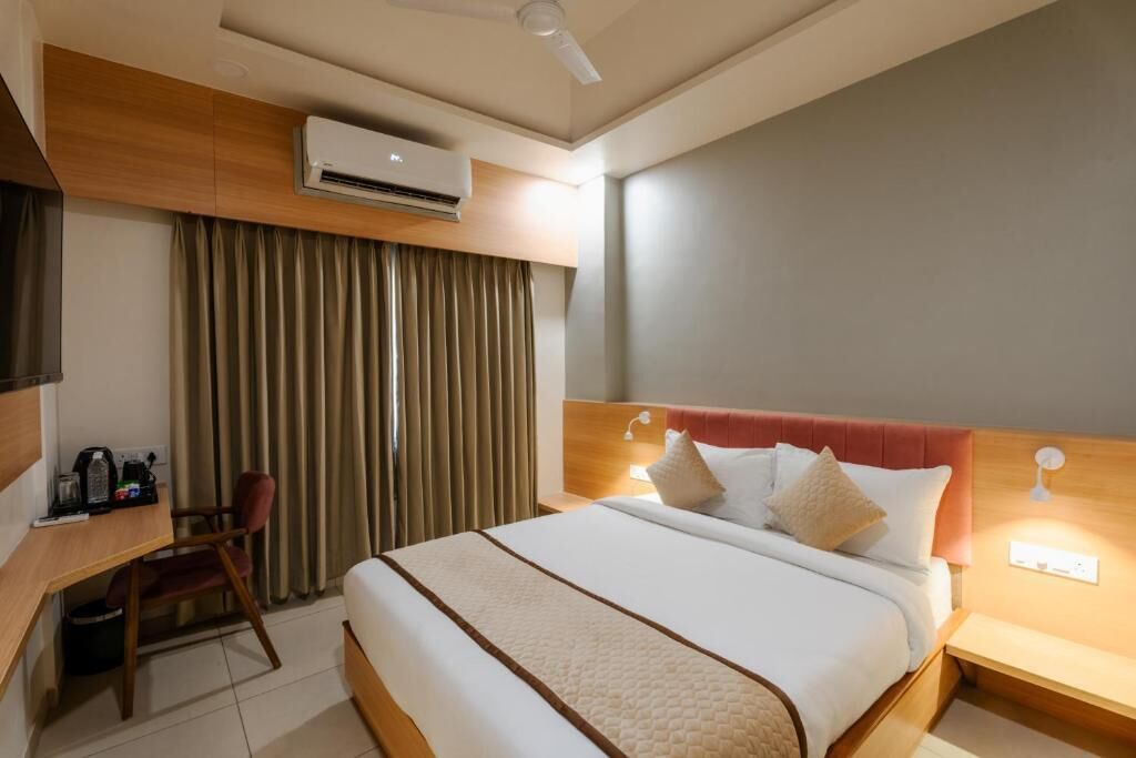 Ein Hotelzimmer mit Bett, Schreibtisch, Stuhl, Klimaanlage und einem Vorhangfenster.