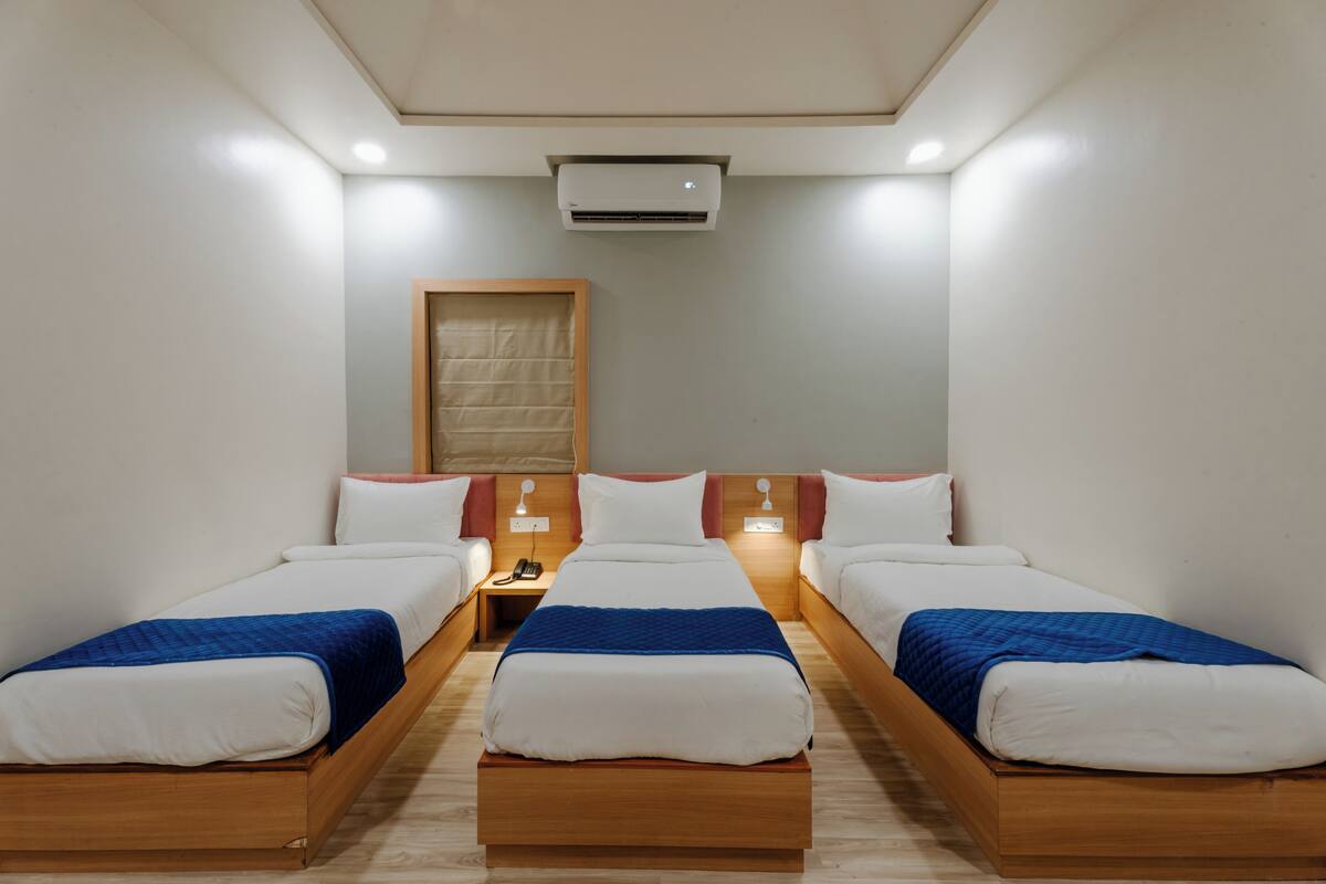 Een hotelkamer met drie enkele bedden, een houten hoofdbord, een nachtkastje met telefoon en een airconditioner.