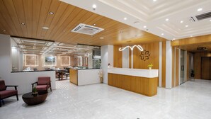 A modern reception area with a wooden ceiling, a reception desk, and a seating area with chairs and a coffee table. - Prarambh By Siara (Nadiad)