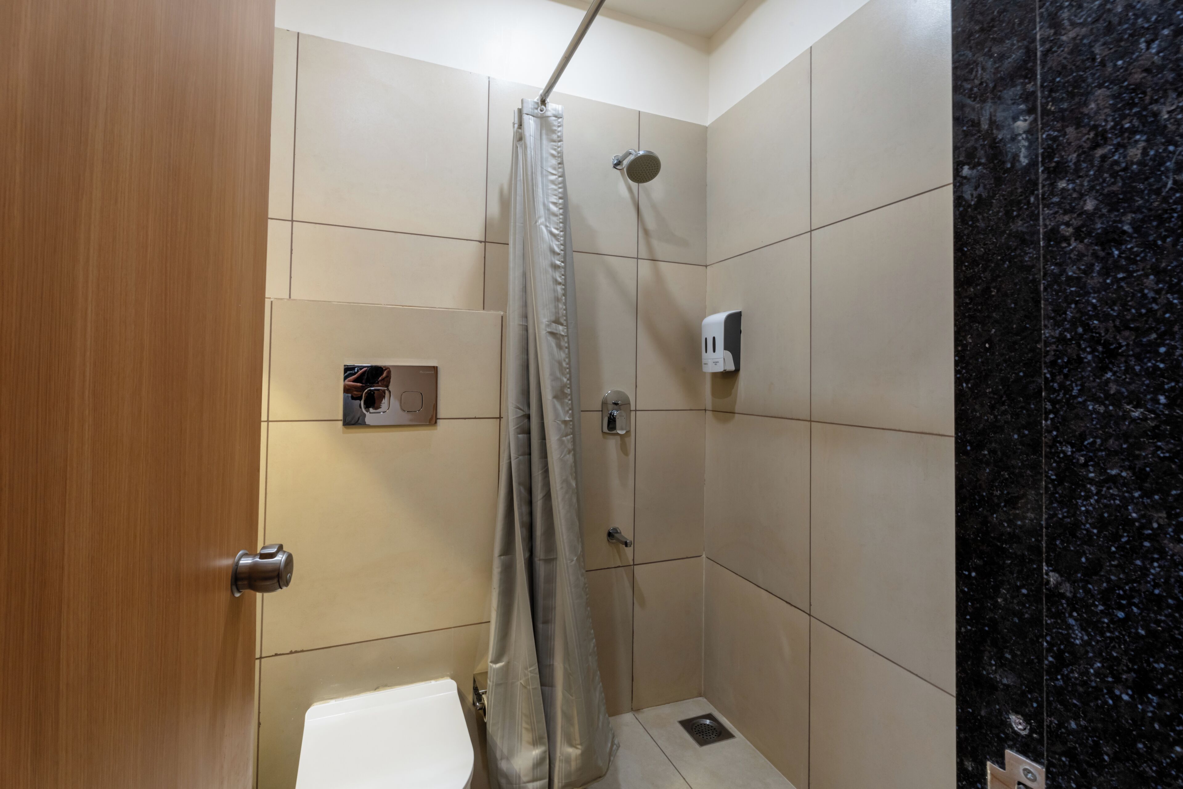 Un baño pequeño con ducha, inodoro y dispensador de jabón.