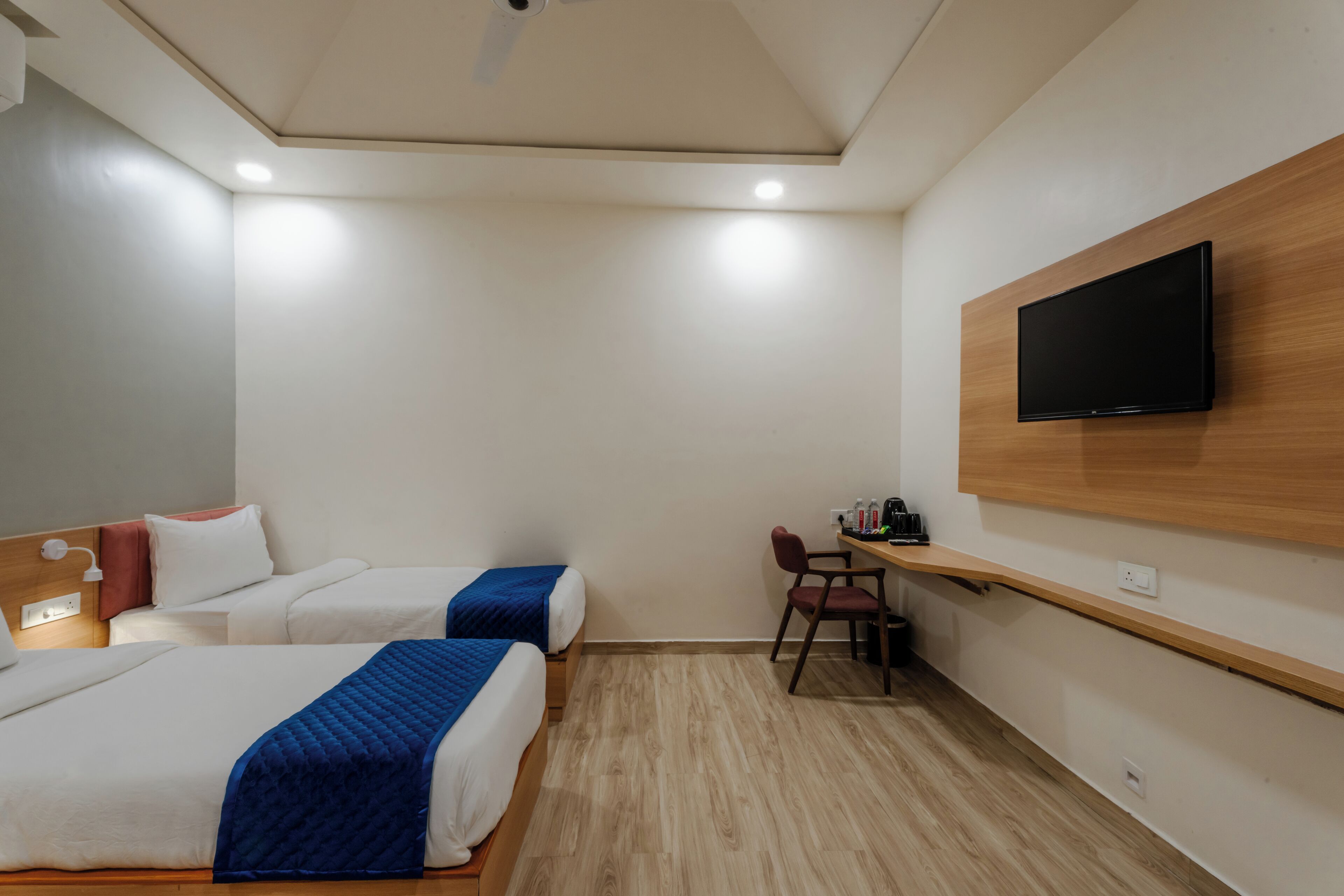 Hotelkamer met twee bedden, een bureau, een stoel, een aan de muur bevestigde televisie en een plafondventilator.