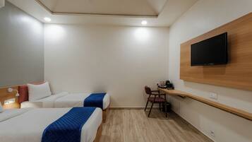 Habitación de hotel con dos camas, un escritorio, una silla, un televisor montado en la pared y un ventilador de techo.
