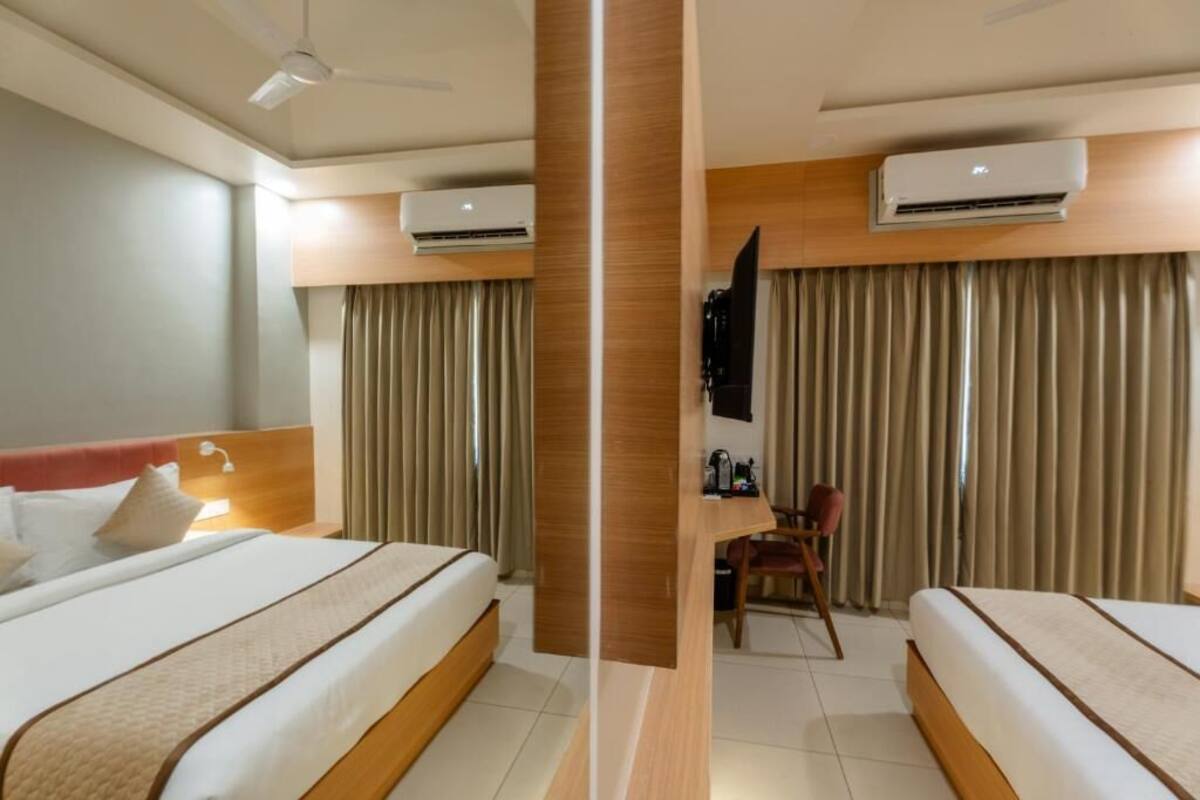 Een hotelkamer met twee bedden, een bureau en een airconditioning op de muur.