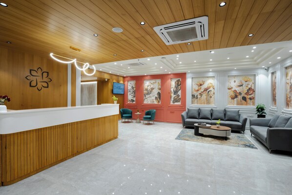 Un área de recepción moderna con un mostrador de madera, sillas color turquesa, sofás grises y un ventanal con motivos florales.