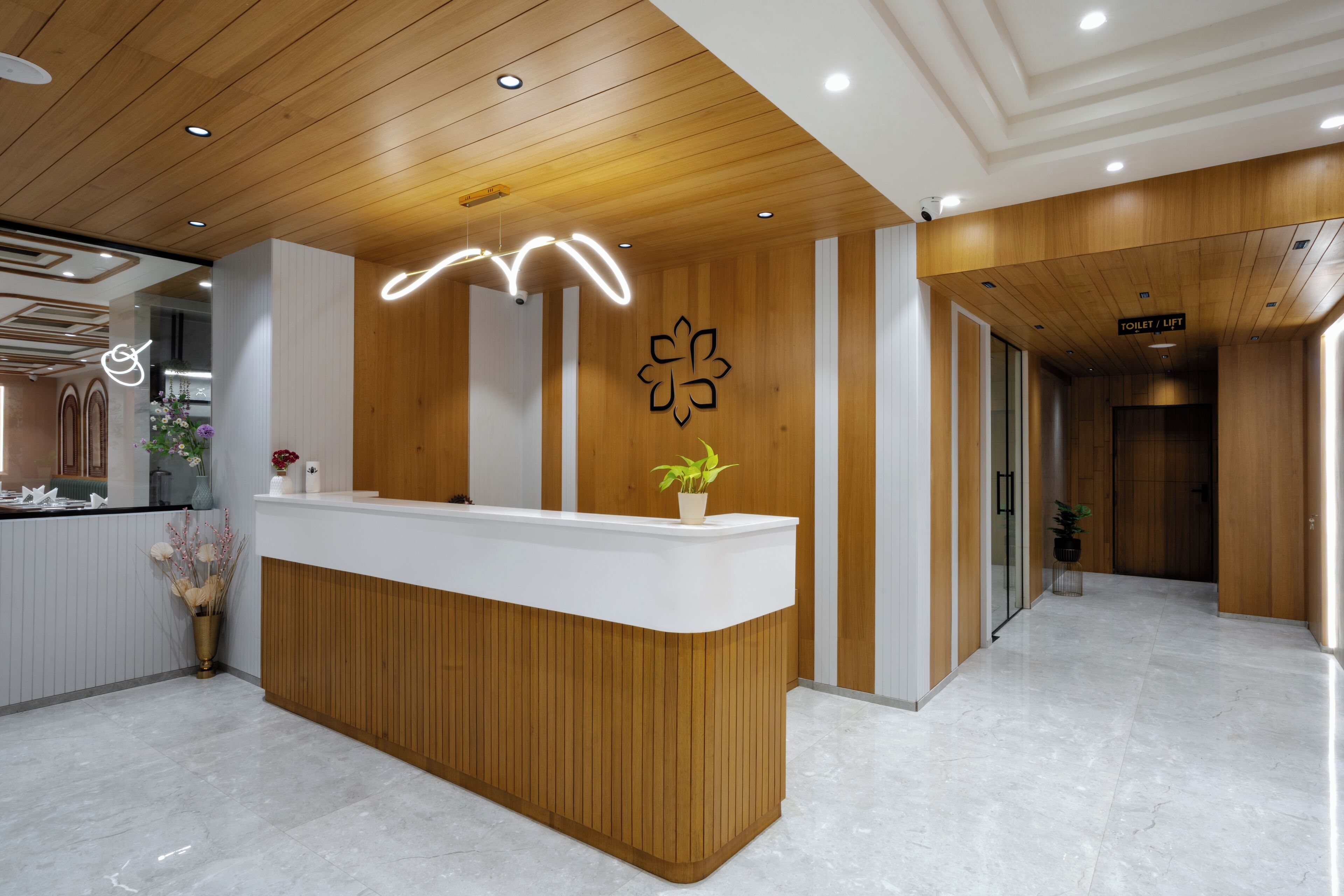 Ein Empfangstresen mit Holzfurnier und einer weißen Arbeitsfläche, eine Wand mit Holzverkleidung und dem Clover-Logo, sowie ein Schild, das eine Toilette und einen Aufzug anzeigt.
