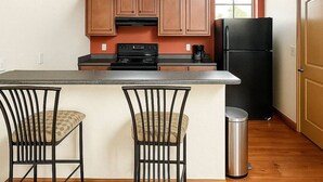 Une cuisine avec des meubles de rangement en bois, un réfrigérateur noir, une cuisinière et deux tabourets de bar.