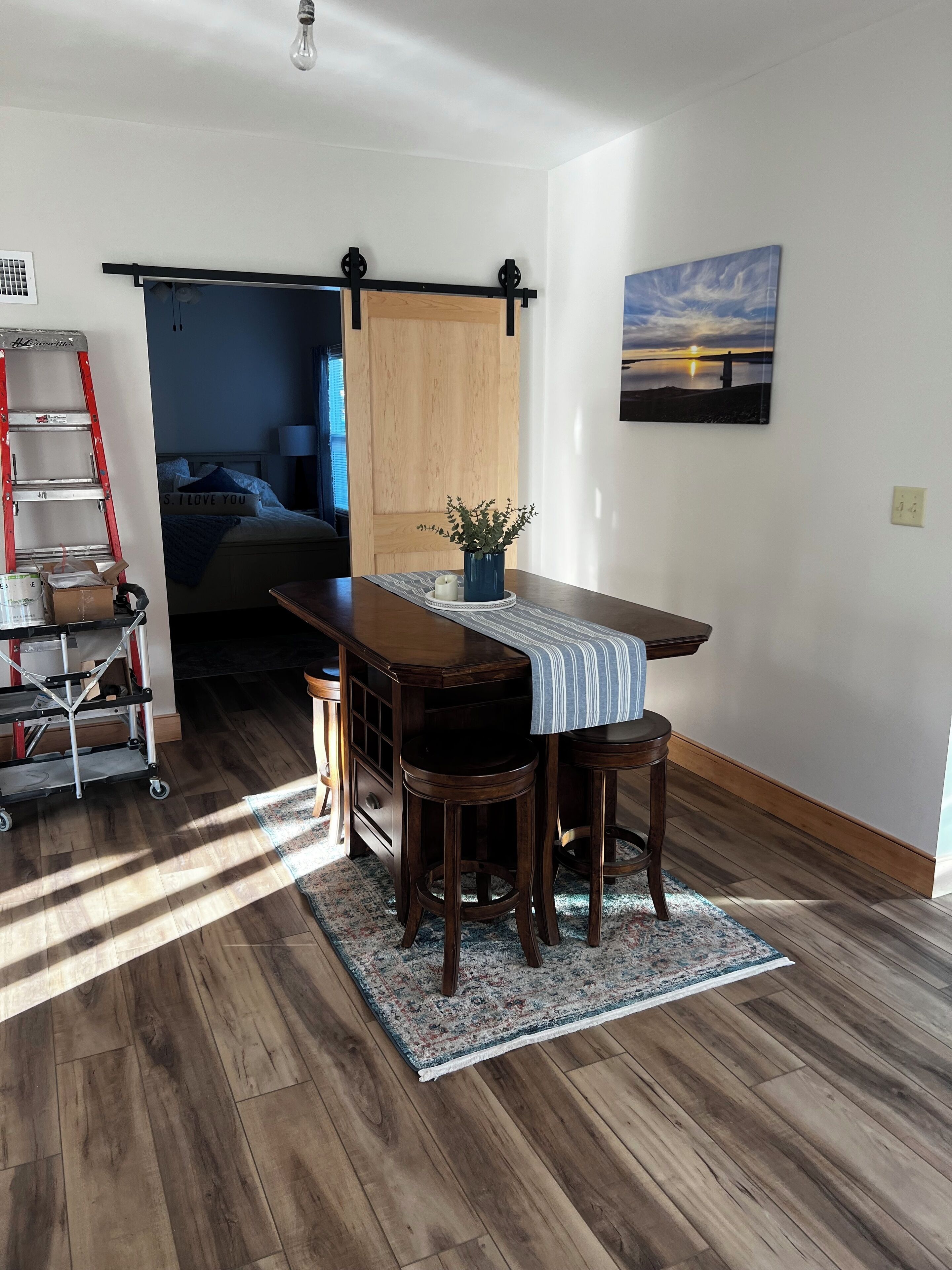 A dining area with a wooden table, two stools, a blue vase with a plant, and a striped table runner.