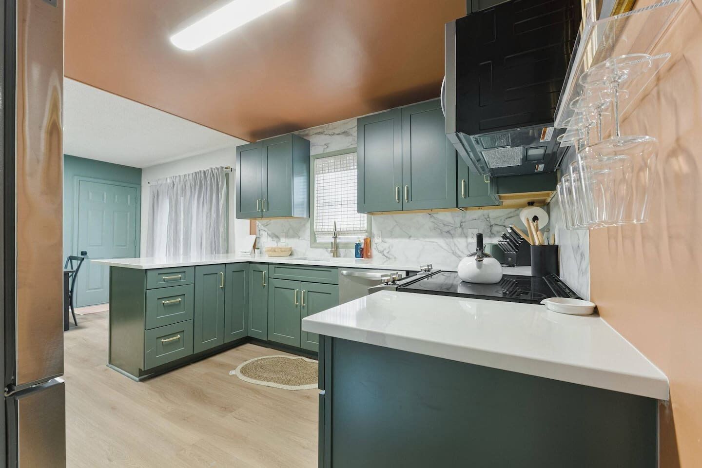 A modern kitchen with green cabinets, a white countertop, and a built-in stove.