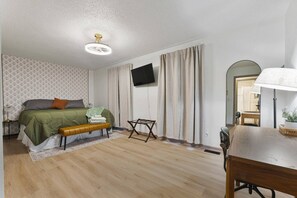 Een slaapkamer met een bed, een bureau, een stoel, een televisie en een plafondventilator.