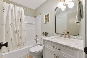Een badkamer met een bad, toilet, wastafel en een douchegordijn met bloemenmotieven.