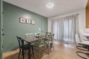 Een eethoek met een tafel en stoelen, een kamerplant en een raam met gordijnen.