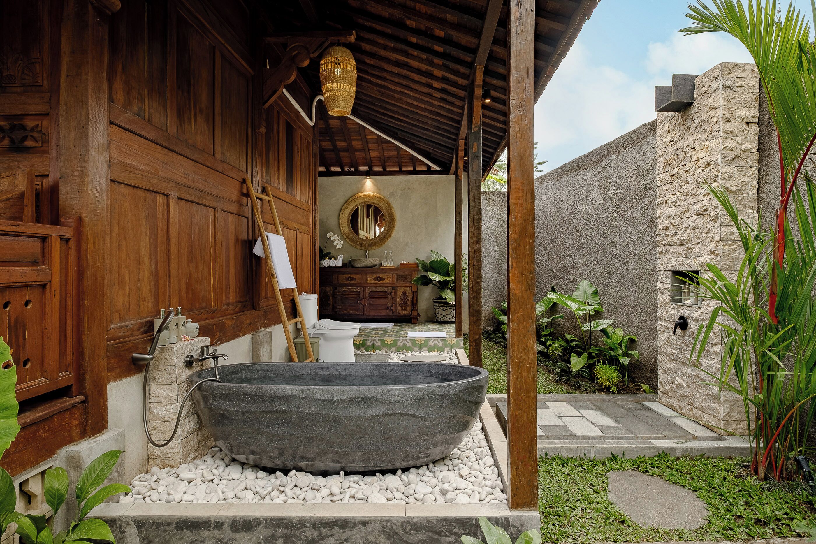 Una construcción rústica de madera con una bañera de piedra grande, una puerta de madera y un muro de piedra.