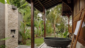 Un espacio de spa con pared de piedra, una bañera negra grande y una terraza de madera.