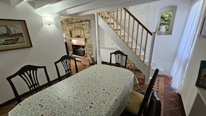 A dining area with a table set for two, a stone fireplace, and a wooden staircase. - Myrtle Cottage - sleeps 4 guests  in 2 bedrooms (St Mawes)