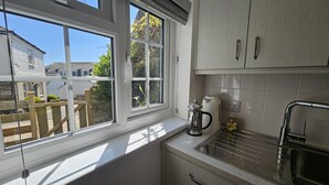A kitchen with white cabinets, a window with a view of houses, a kettle, and a sink. - Myrtle Cottage - sleeps 4 guests  in 2 bedrooms (St Mawes)