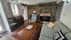 A cozy living room with a stone fireplace, a grey sofa, a wooden coffee table, and a blue armchair. - Myrtle Cottage - sleeps 4 guests  in 2 bedrooms (St Mawes)