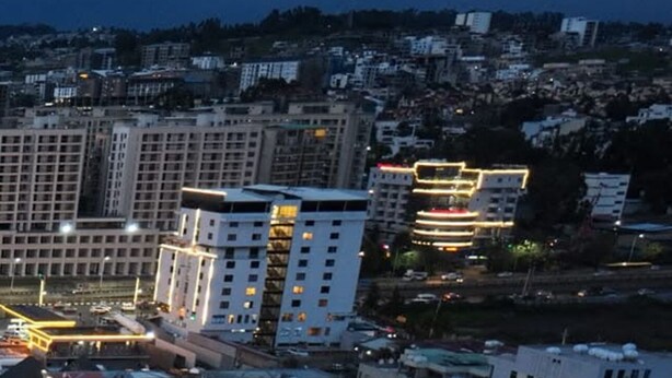 Une zone urbaine avec un terrain de basket entouré de bâtiments, dont certains ont des fenêtres illuminées.