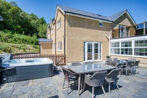 Ein Haus mit einer Terrassenanlage, die ein Whirlpool, Sitzmöglichkeiten im Freien und ein großes Fenster bietet.