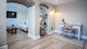 A living room with a stone archway, a white sofa, a coffee table, a TV, and a wooden desk with a chair.