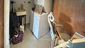 Una habitación pequeña con ventilador de techo, refrigerador blanco, armario de madera, lavamanos y un trapeador.