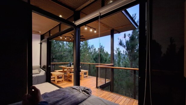 Un interior moderno con balcón, muebles de madera y vistas a árboles.