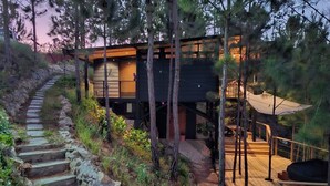 Una casa moderna con una escalera que lleva a una terraza de madera, rodeada de árboles.