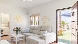 Un salon moderne avec un canapé d’angle beige, une table basse blanche et une vue sur le jardin grâce à une porte-fenêtre coulissante.
